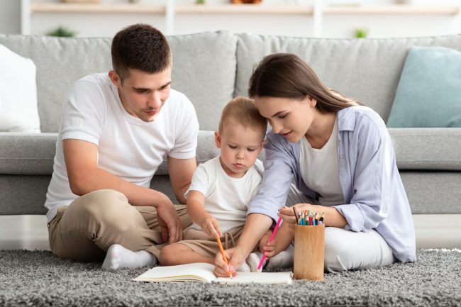 Young Parents With Adorable Infant Baby Drawing Together At Home